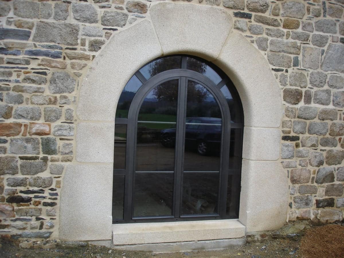 Fenêtre aluminium Arabesk cintrée (plein cintre) anthracite dans un mur en pierre