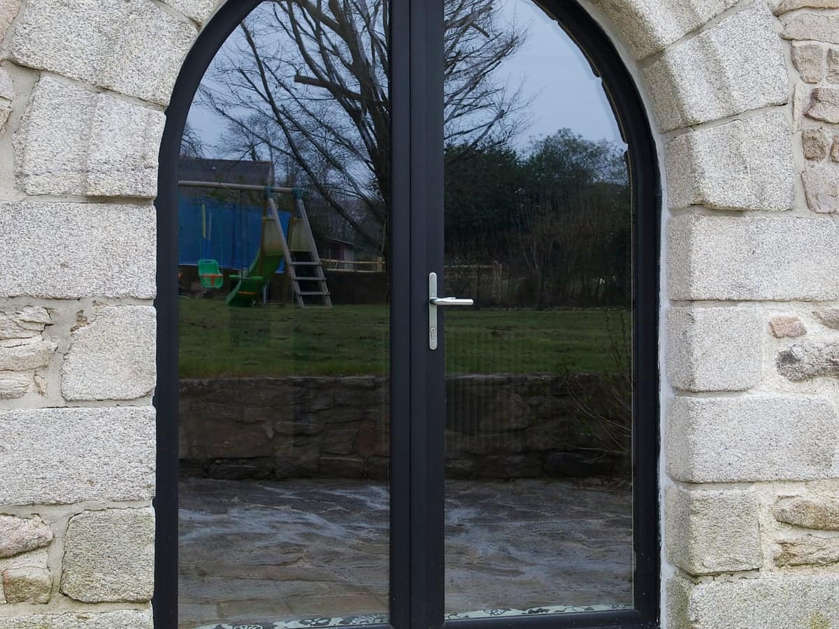Fenêtre bois-aluminium Karat cintrée anthracite dans un mur en pierre