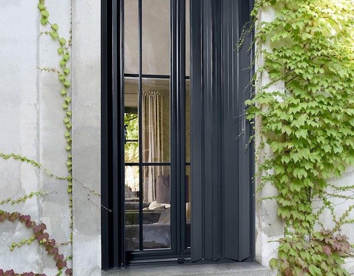 Persienne pliante aluminium anthracite KparK sur une façade en pierre couverte de lierre