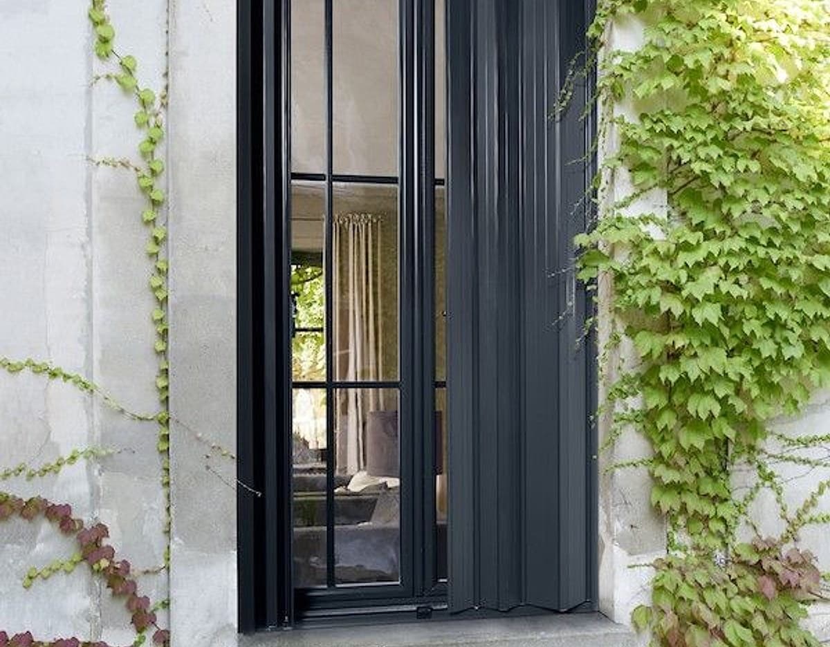 Persienne pliante aluminium anthracite KparK sur une façade en pierre couverte de lierre