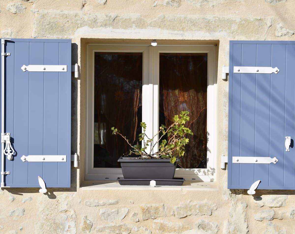 Volets battants aluminium bleus KparK sur une façade en pierre